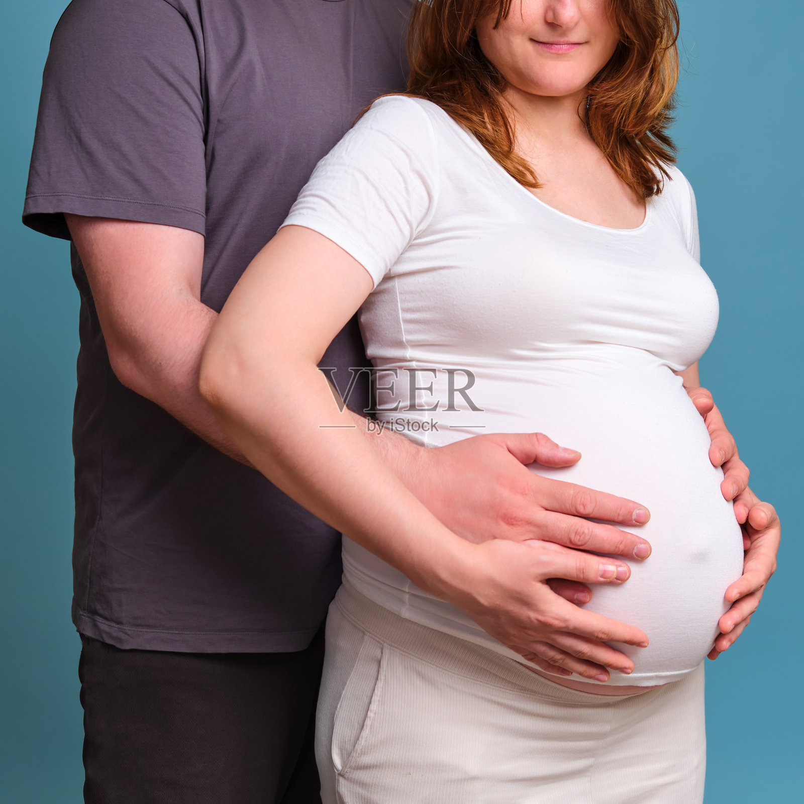 丈夫将手放在怀孕妻子的肚子上,蓝色背景上的工作室照片照片摄影图片