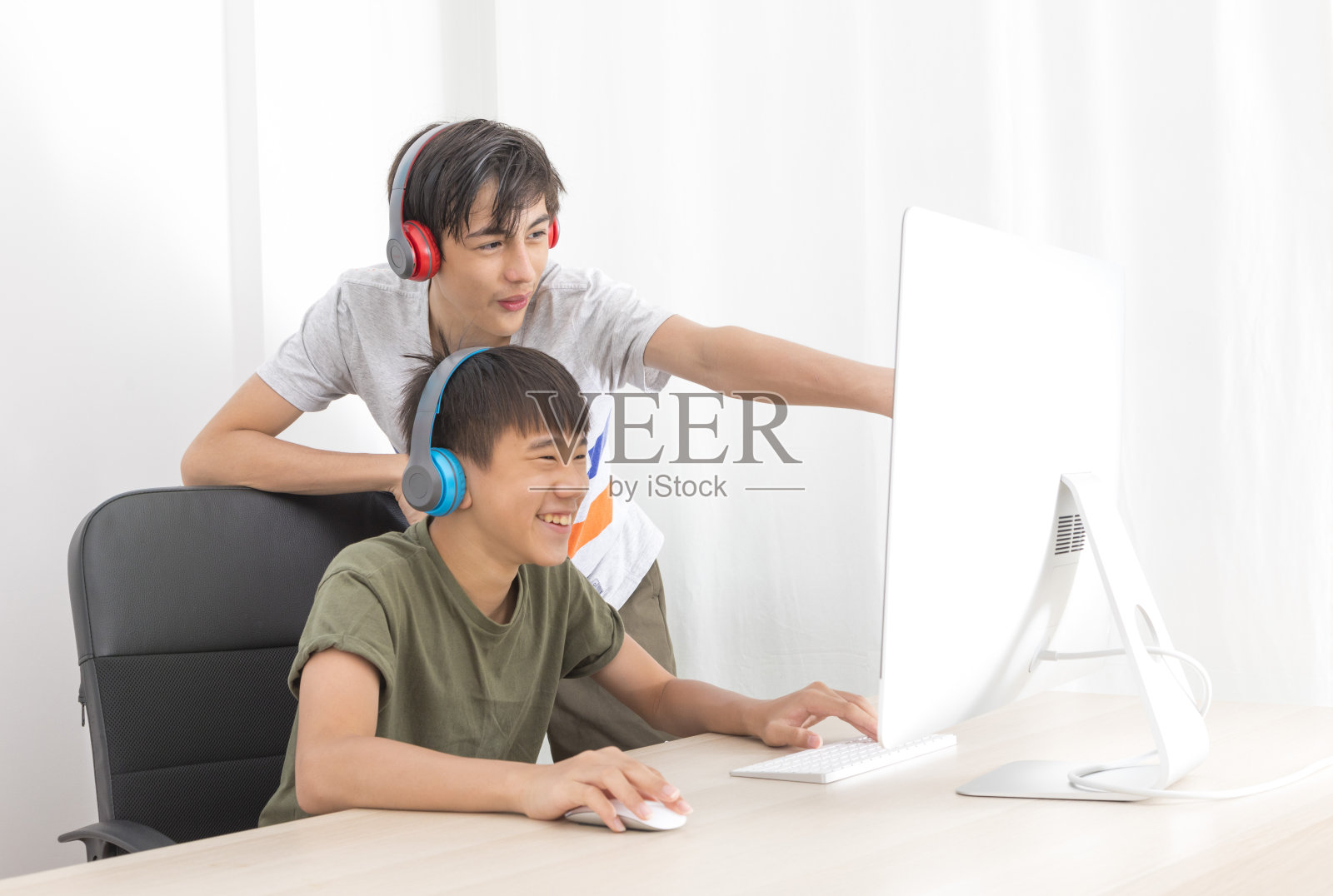 两个十几岁的男孩戴着耳机在家玩网络游戏。照片摄影图片