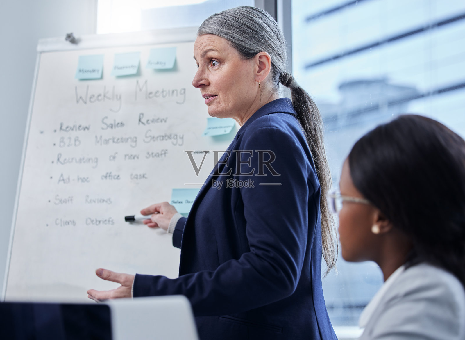 这张照片是一位成熟的女商人在办公室里用白板给同事做演示照片摄影图片