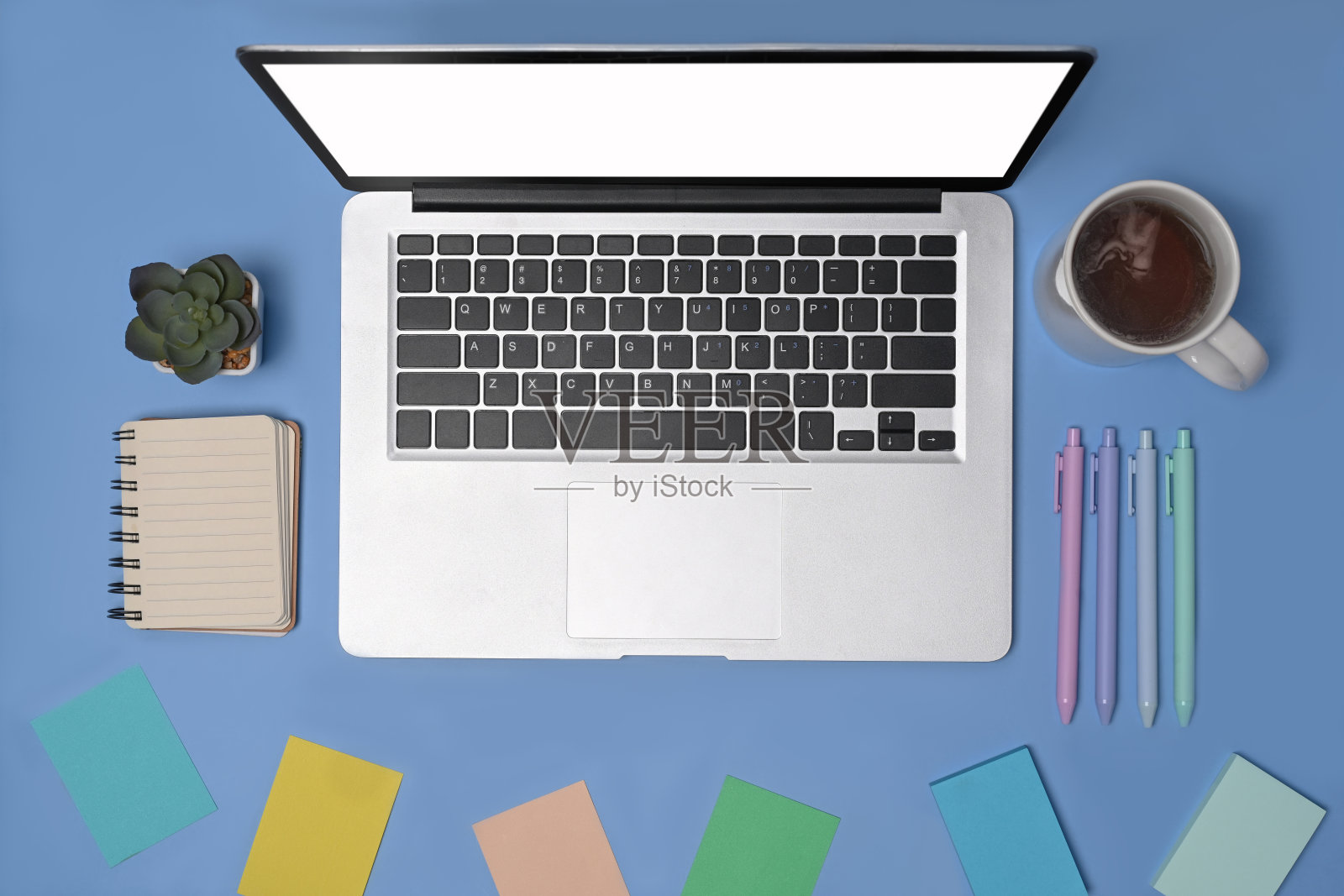头顶拍摄的笔记本电脑,咖啡杯和便利贴在蓝色的背景照片摄影图片