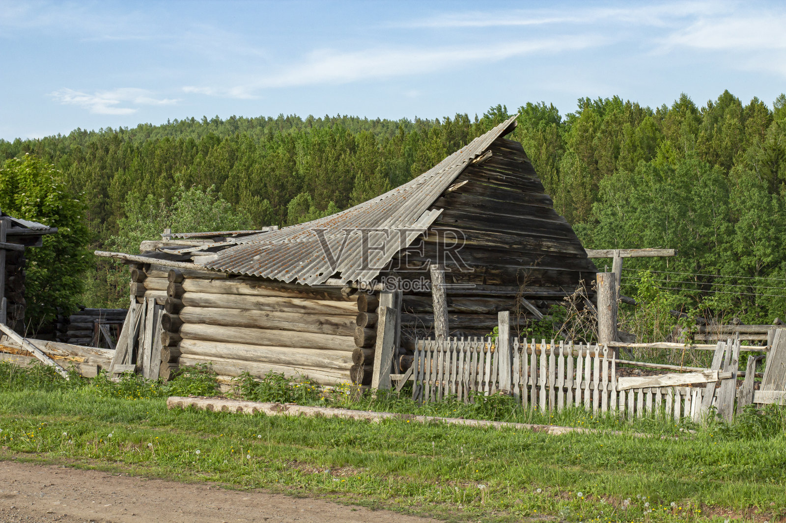 一个废弃的原木谷仓和一个村庄的篱笆的一部分,在一个明亮的绿色背景在夏天照片摄影图片