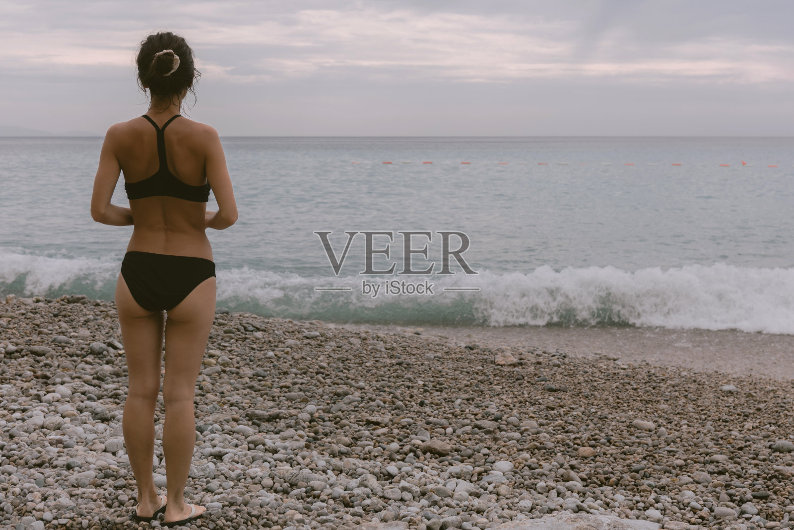 年轻女性穿着比基尼站在海滩上,看着大海。照片摄影图片