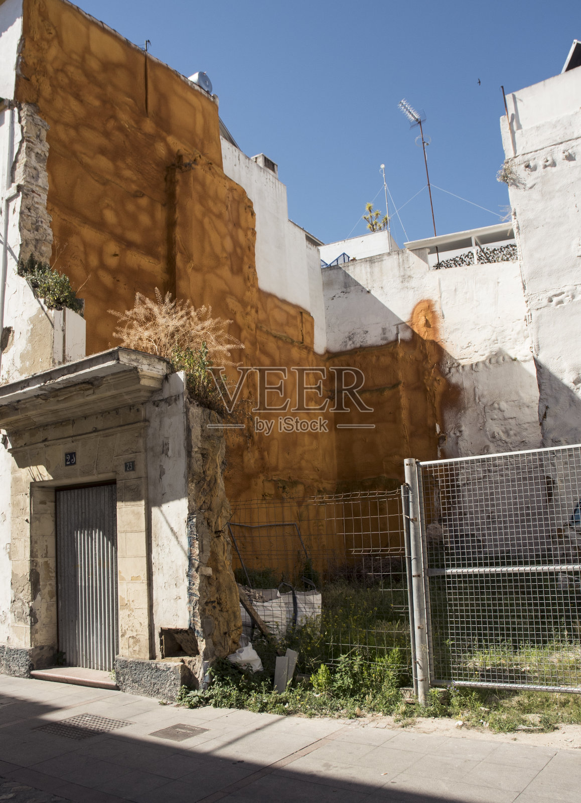 镇上街道上的空地,等待施工用金属网保护,左边墙上有橙色的绝缘体照片摄影图片