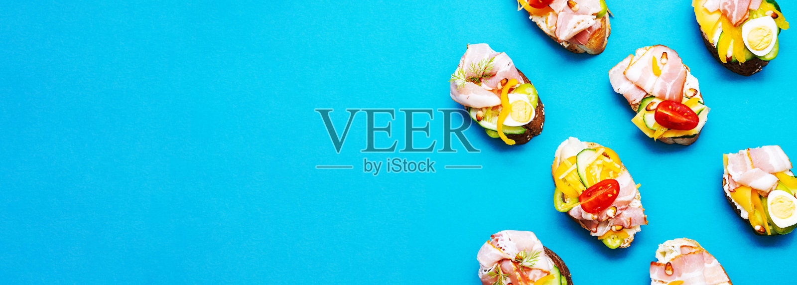 流行的开放式三明治有奶油芝士,鹌鹑蛋,西红柿,培根和蔬菜。现代,夏季静物生活的健康零食。平铺在极简主义风格。有各种馅料。照片摄影图片