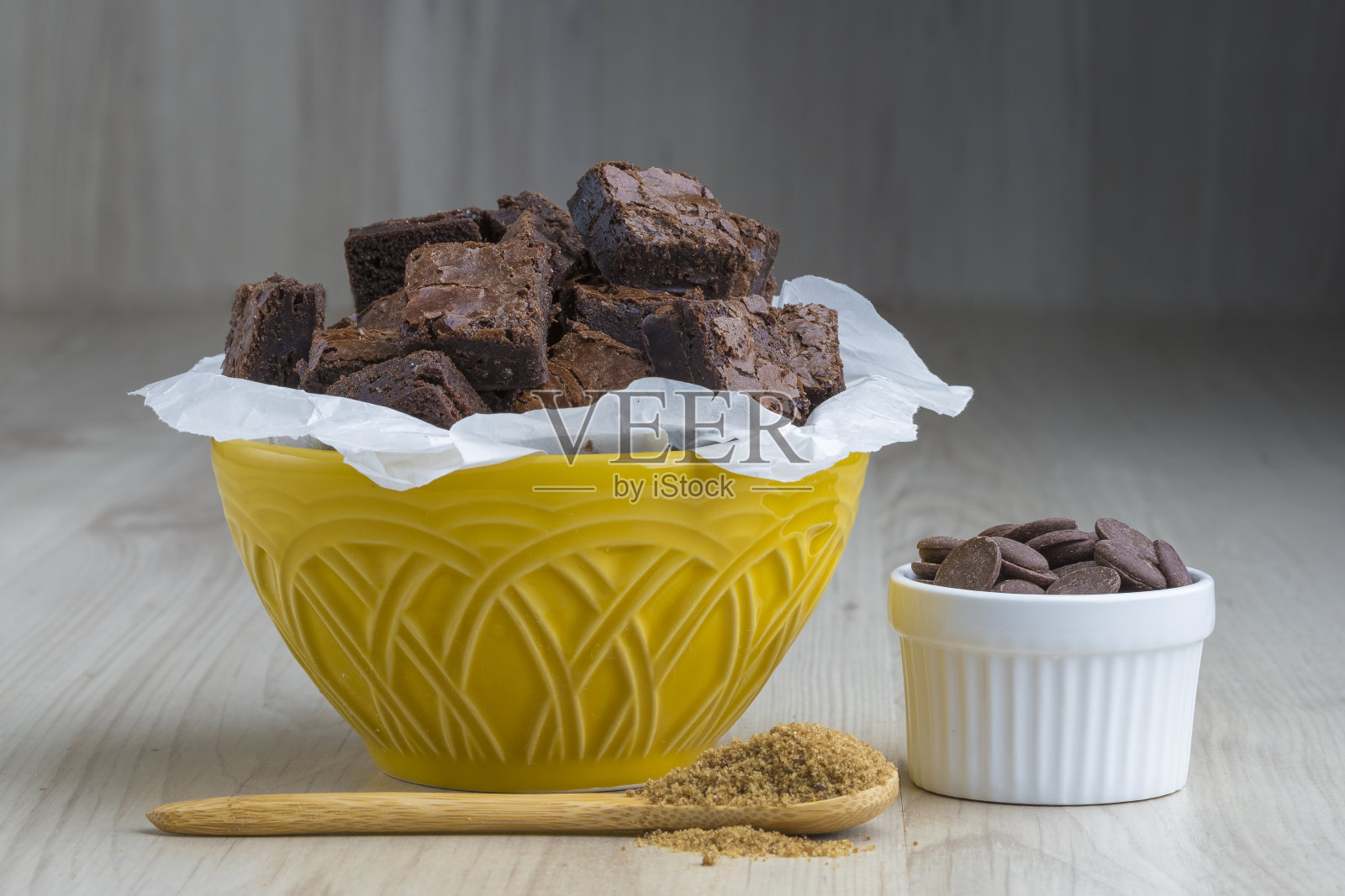把布朗尼切成丁,放在一个黄色的碗里,碗底是木制的,碗上装饰着红糖和巧克力硬币,照片摄影图片