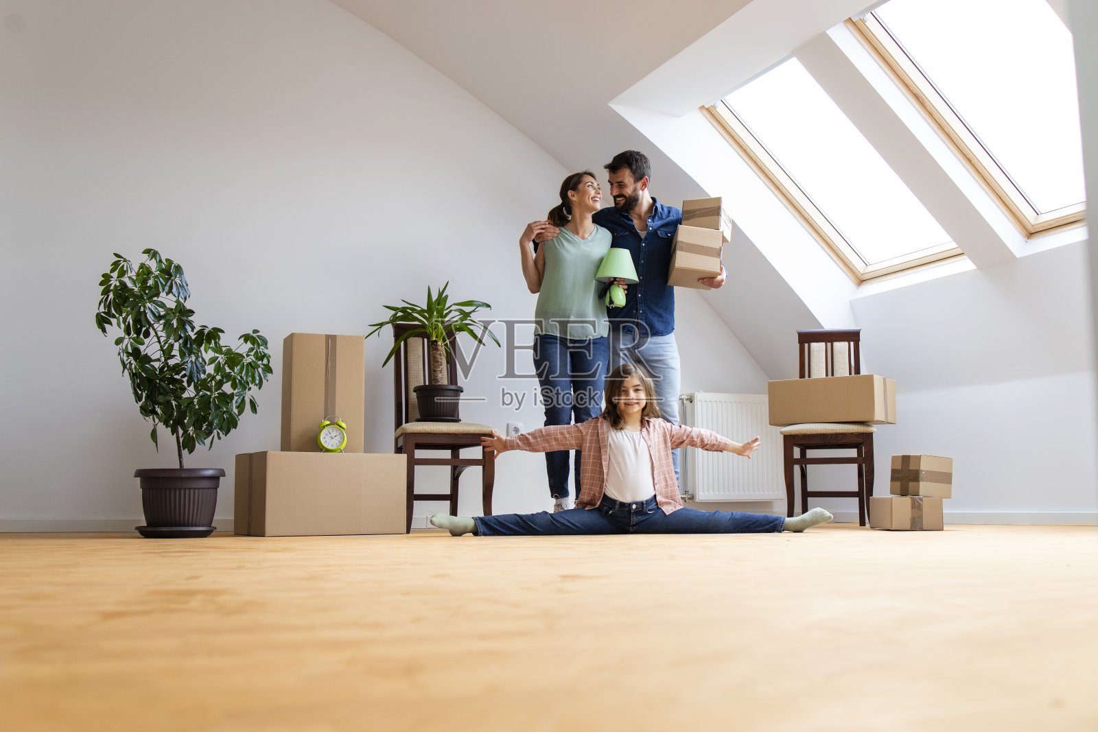 一个幸福的白人家庭搬进了新公寓,灵活的小女孩在做体操,父母在搬运行李。照片摄影图片