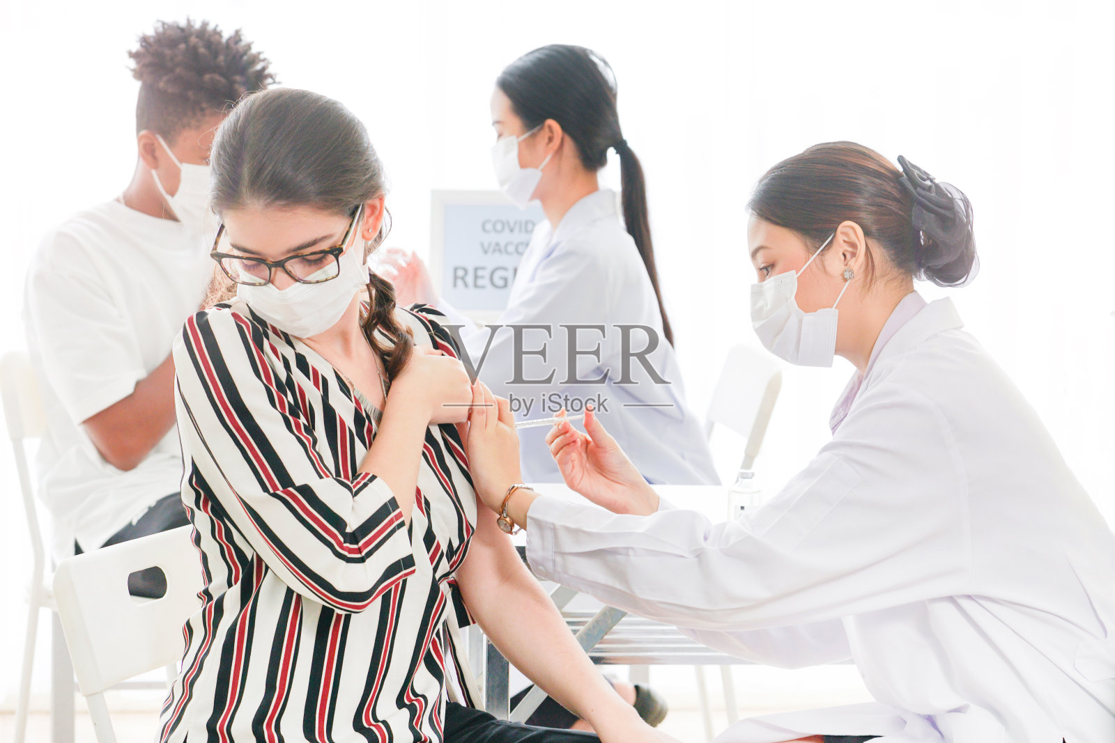 在诊所或医院接种冠状病毒疫苗者。佩戴防护口罩的女性。医务人员和护士使用注射器给手臂注射疫苗。照片摄影图片