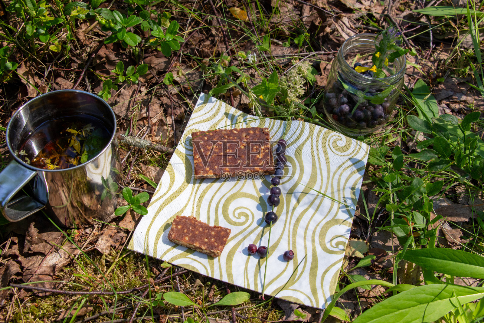 在阳光明媚的夏日里,搭配谷物能量棒、新鲜黑莓、金属杯凉茶的森林小吃照片摄影图片