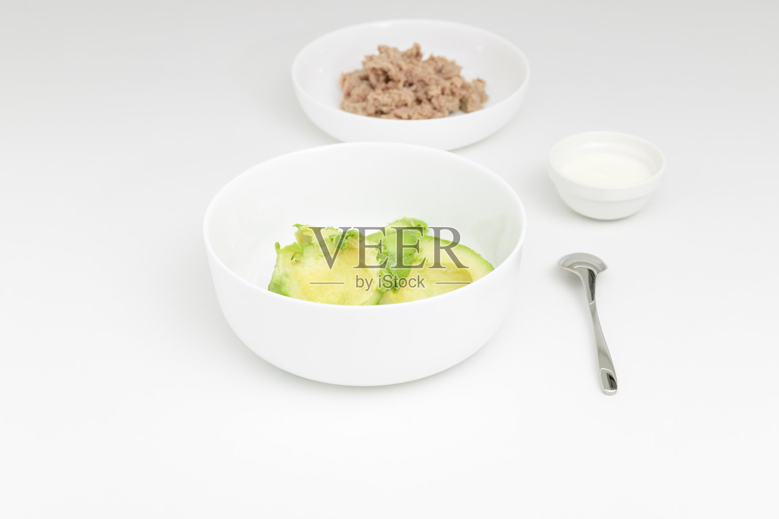 白盘子里去皮的牛油果。背景是酸奶和金枪鱼。一步一步的配方。照片摄影图片