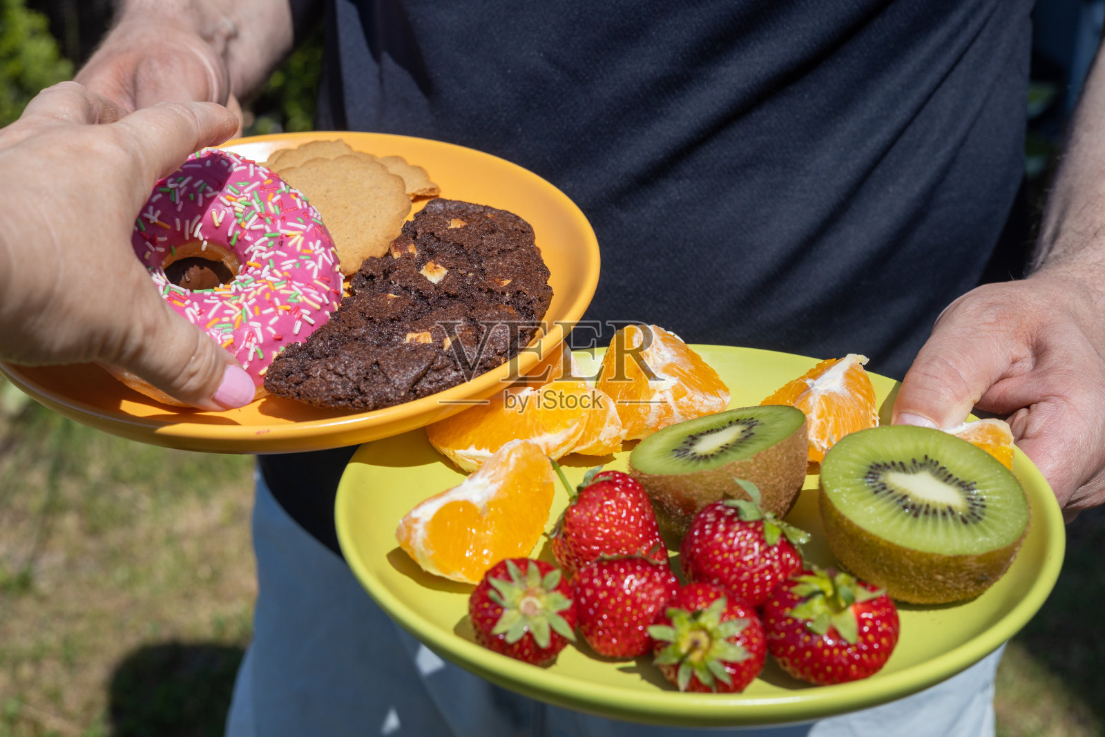 健康或不健康,膳食,两个盘子可以选择水果和饼干,一只手去拿甜甜甜圈,而不是健康的食物照片摄影图片
