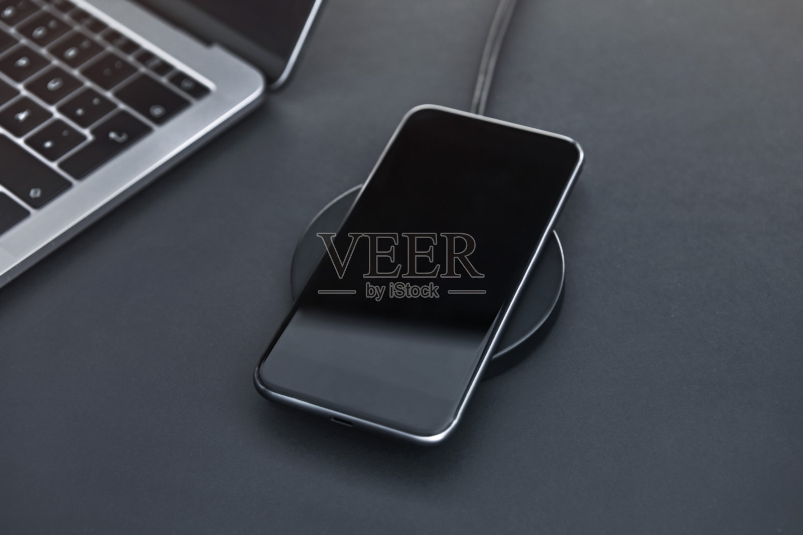 工作时间在办公室给豪华智能手机充电。深灰色的书桌上。照片摄影图片