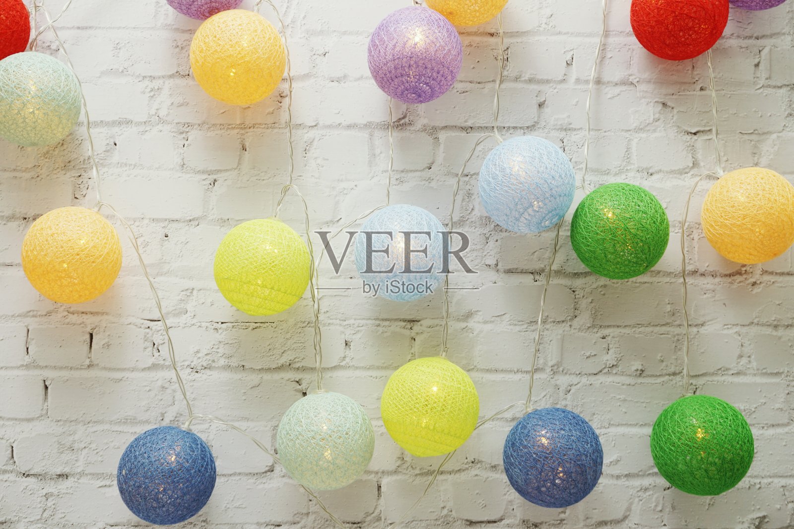 彩色LED棉球装饰在白色砖墙背景上照片摄影图片