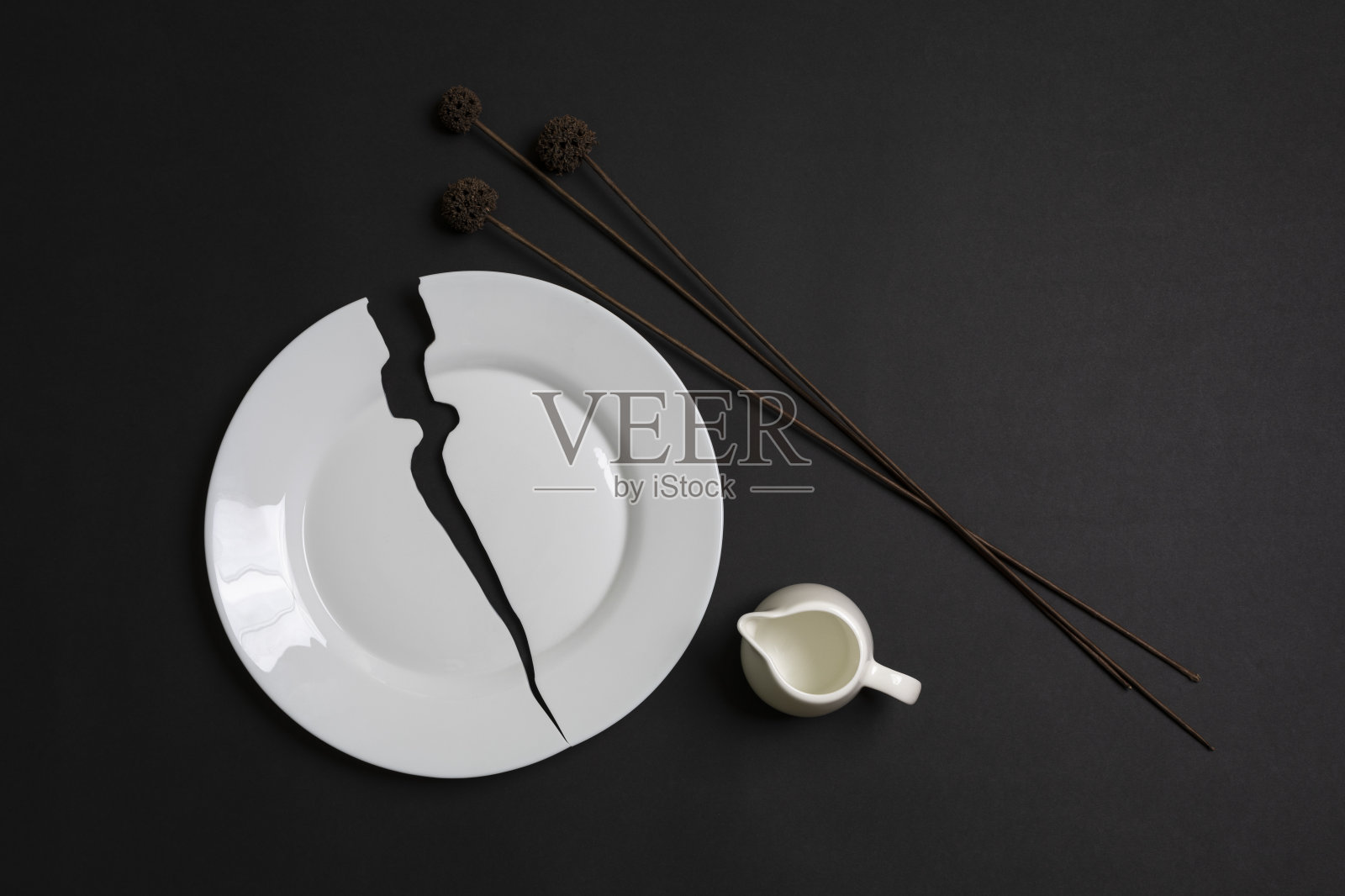 一个白色的碎盘子和一朵干花在黑色的背景上。照片摄影图片