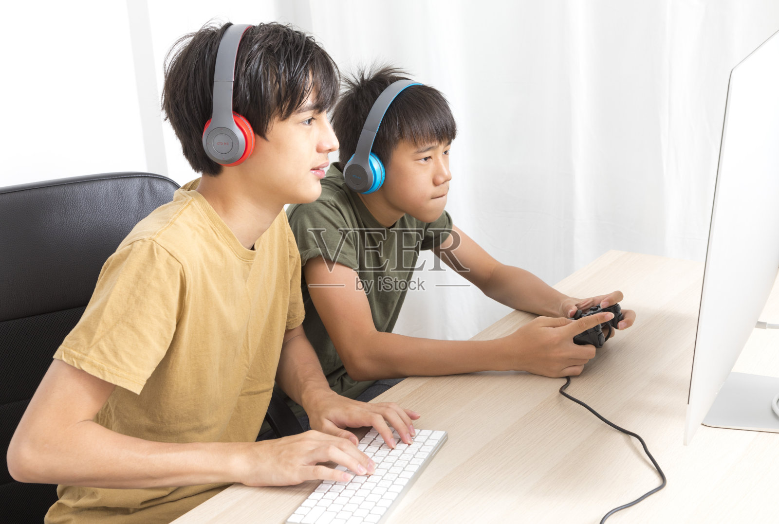 两个十几岁的男孩戴着耳机在家玩网络游戏。照片摄影图片