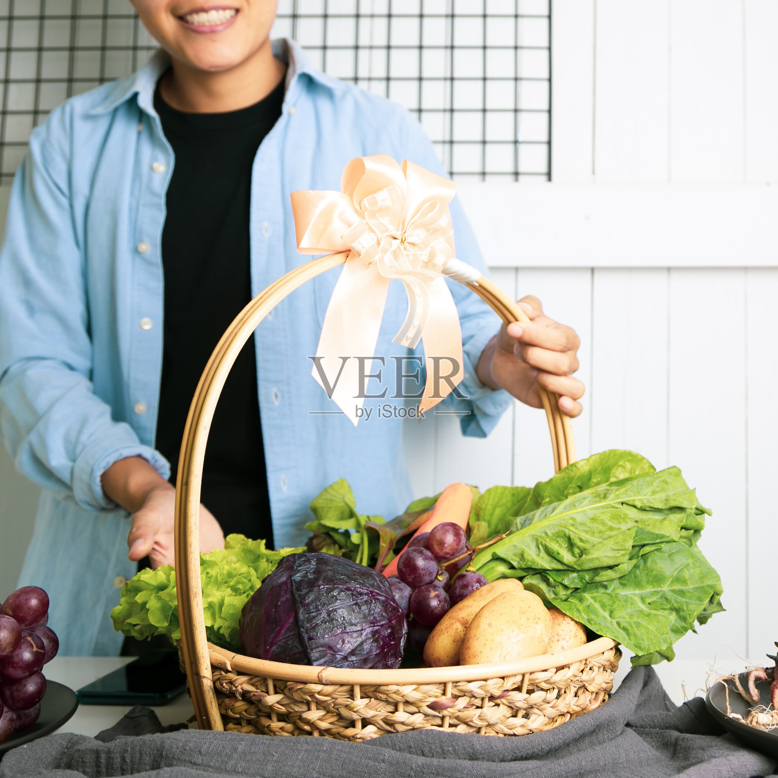一个穿着蓝色衬衫的男人拿着一篮子新鲜的蔬菜,羽衣甘蓝,土豆,紫甘蓝和葡萄。送给你健康的礼物照片摄影图片