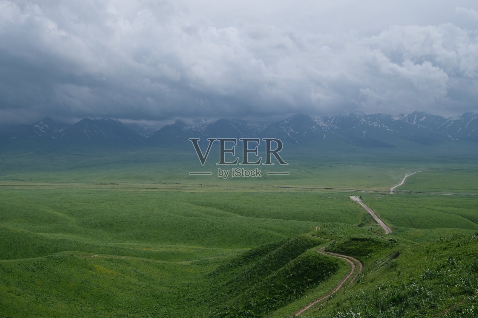 苍翠的草原,在多云的天空下,有一条通向山脉的长路照片摄影图片