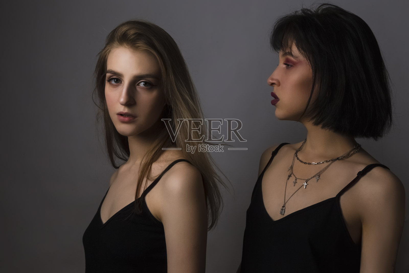 一对白人女孩与明亮的化妆在灰色的背景摆姿势。水平的形象照片摄影图片