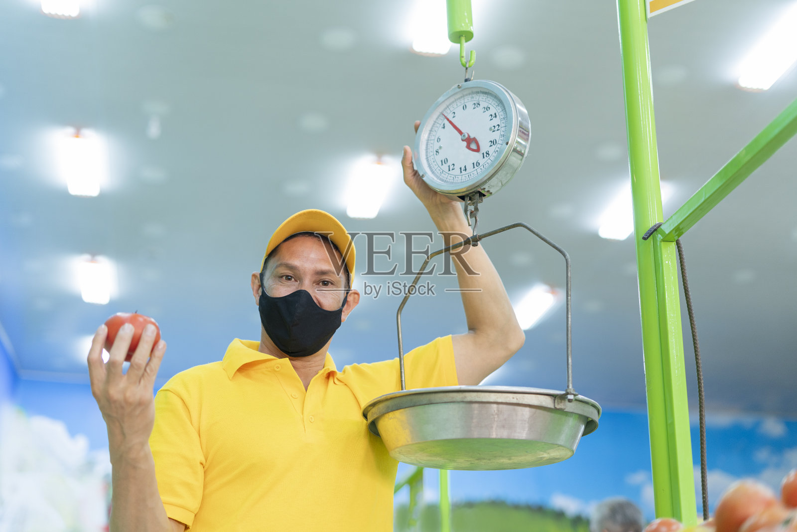 蔬菜水果店的店员穿着制服,戴着睫毛膏,一边摆水果,一边微笑着看着相机的肖像。照片摄影图片