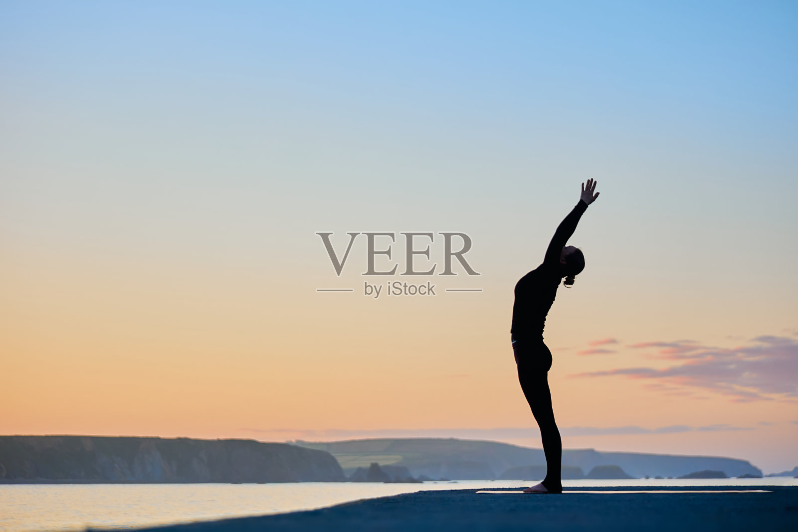 一个女人在海边做瑜伽体式在一个美丽的日出照片摄影图片