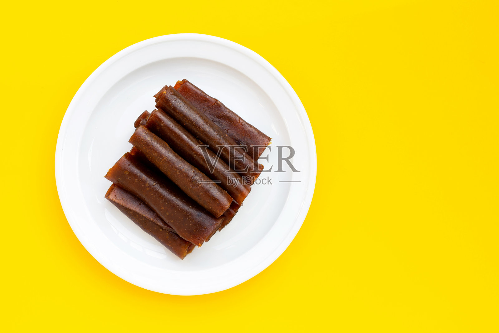 干芒果酱在白色盘子上黄色的背景。照片摄影图片