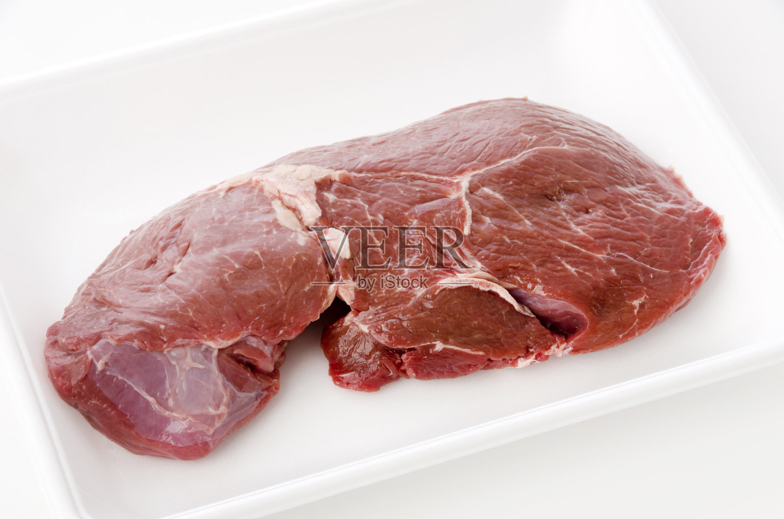 泡沫盘上的圆牛排,背景是白色。照片摄影图片