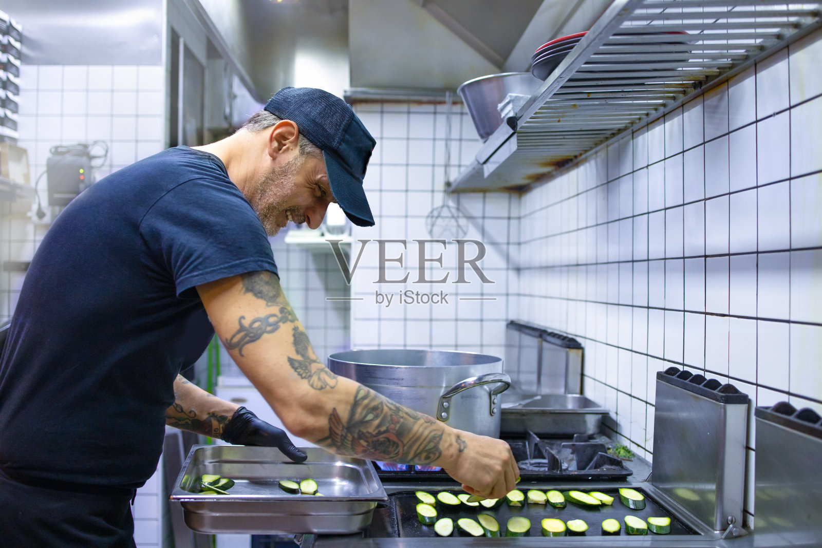 在他的餐厅里,年轻的厨师在铸铁煎锅上准备烤蔬菜。健康食品制备理念。照片摄影图片