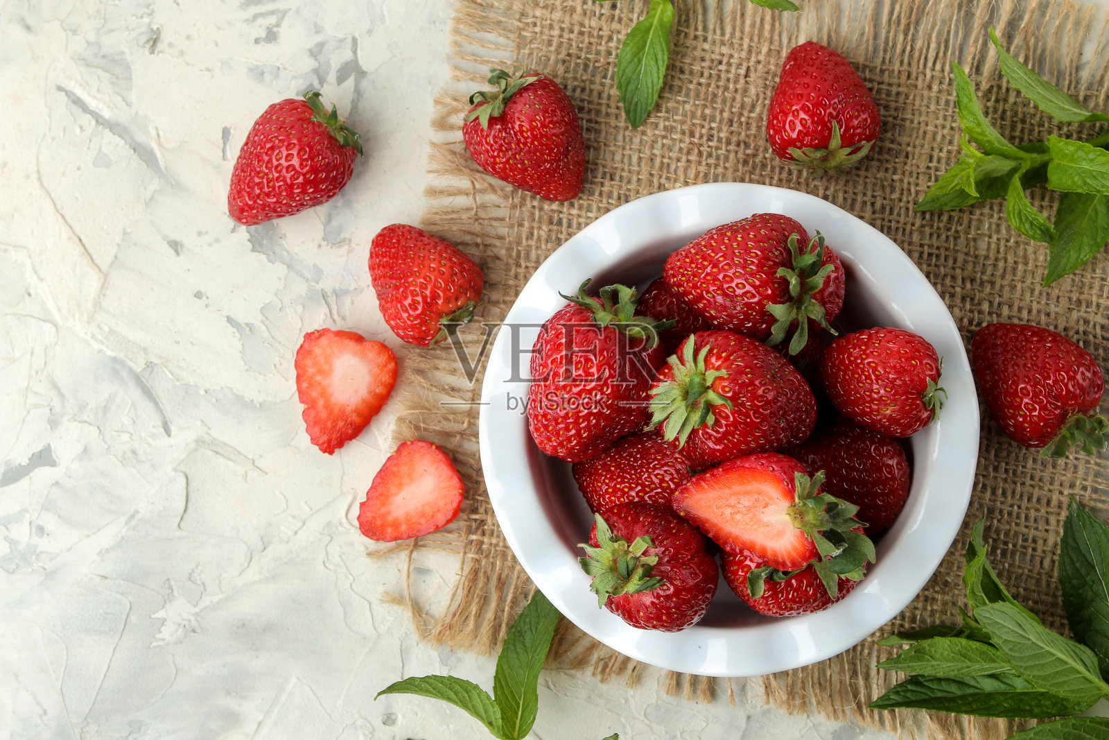 成熟,美味的草莓。红色草莓装在陶瓷碗里,放在一个轻混凝土桌子上。俯视图照片摄影图片