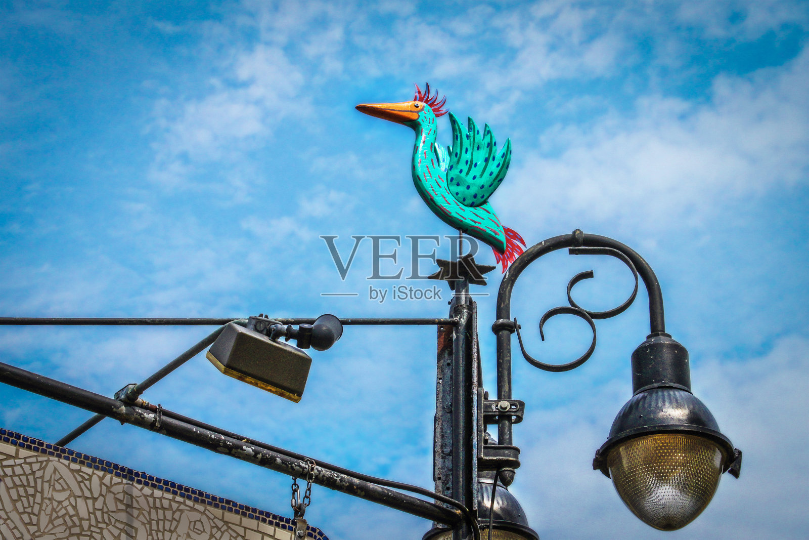 在时髦的位置上,漆木绿松石鸟安装在肮脏的金属标志和灯柱下斑驳的蓝色云天空照片摄影图片