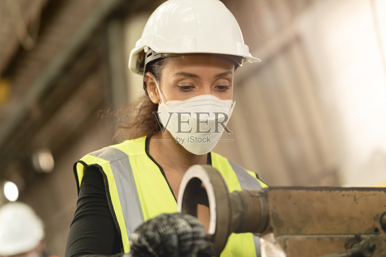 工人工厂巴西妇女戴着面罩和工作在重型机器。空气污染、烟尘和冠状病毒病的安全防护。工作场所的新常态。照片摄影图片