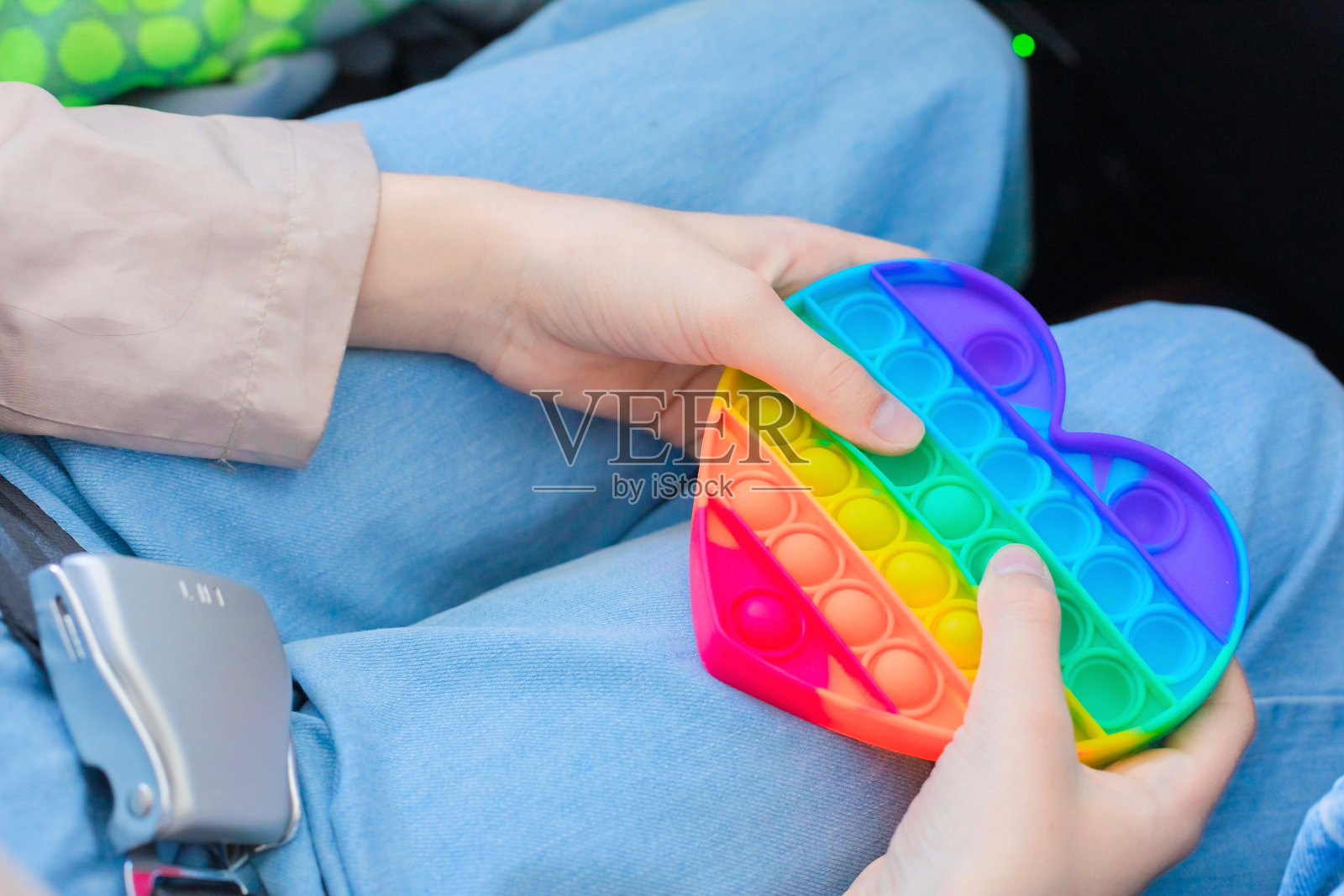 蓝色牛仔裤背景上的一个女孩手里拿着一个彩虹色的波比特玩具。对飞行的恐惧。照片摄影图片