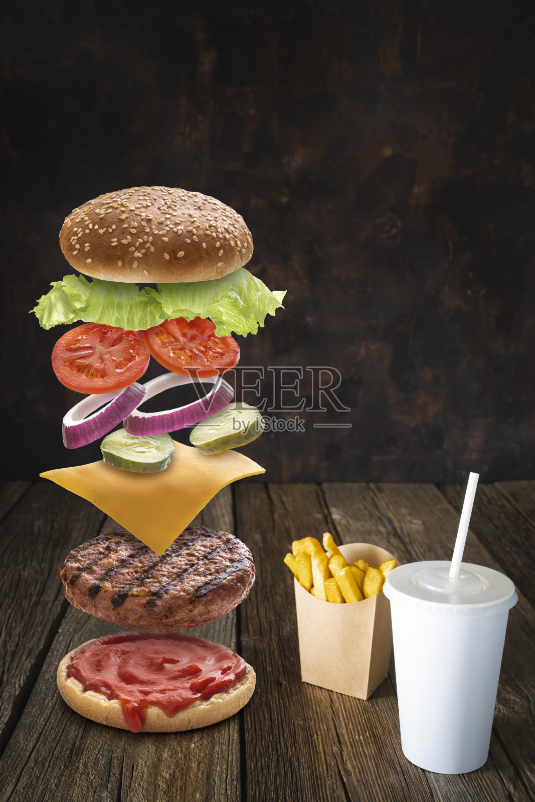 汉堡配料搭配薯条和一次性饮料纸杯放在深色的木头上照片摄影图片