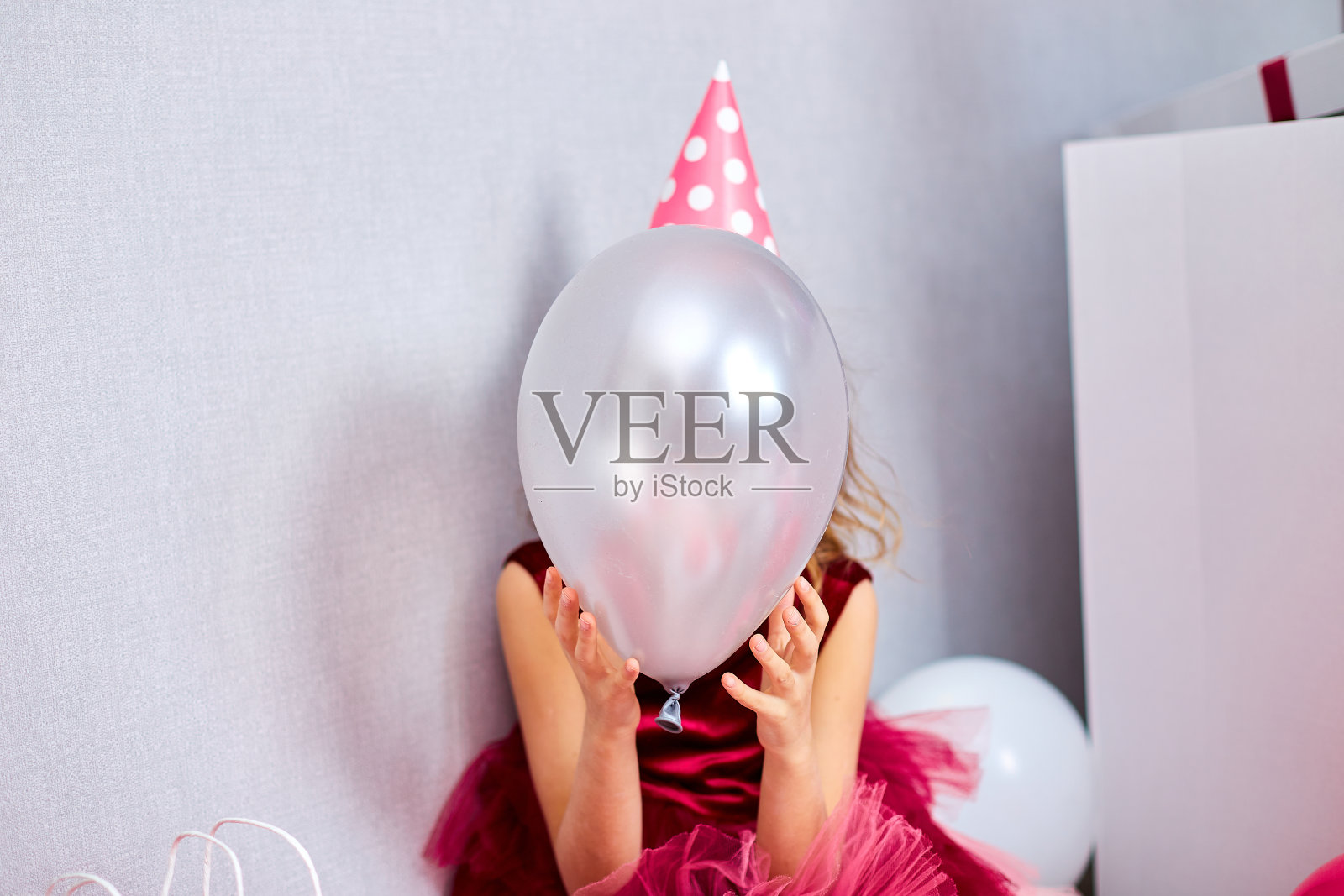 快乐的小寿星穿着粉红色的裙子和帽子用气球遮住了他的脸在家庭聚会照片摄影图片