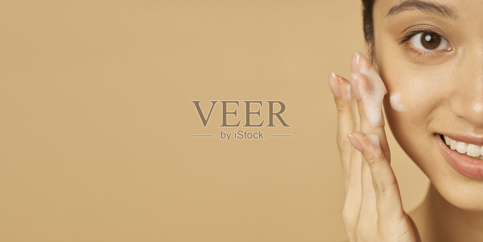 工作室的网站标题美丽的年轻女子在镜头前微笑的半边脸肖像,同时应用温和的泡沫洁面乳隔离米色背景照片摄影图片