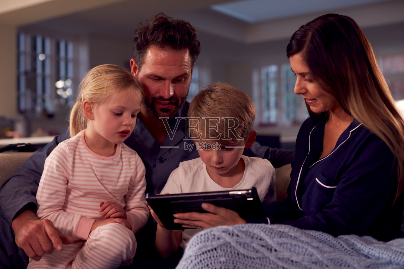 穿着睡衣的家人坐在沙发上一起看平板电脑照片摄影图片