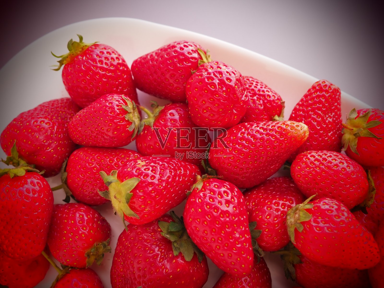 盘子上的草莓,灰色背景。白色的菜肴和美味的红色大花园草莓。健康的食物,维生素和素食。有食物的静物。副本的空间。平躺照片摄影图片