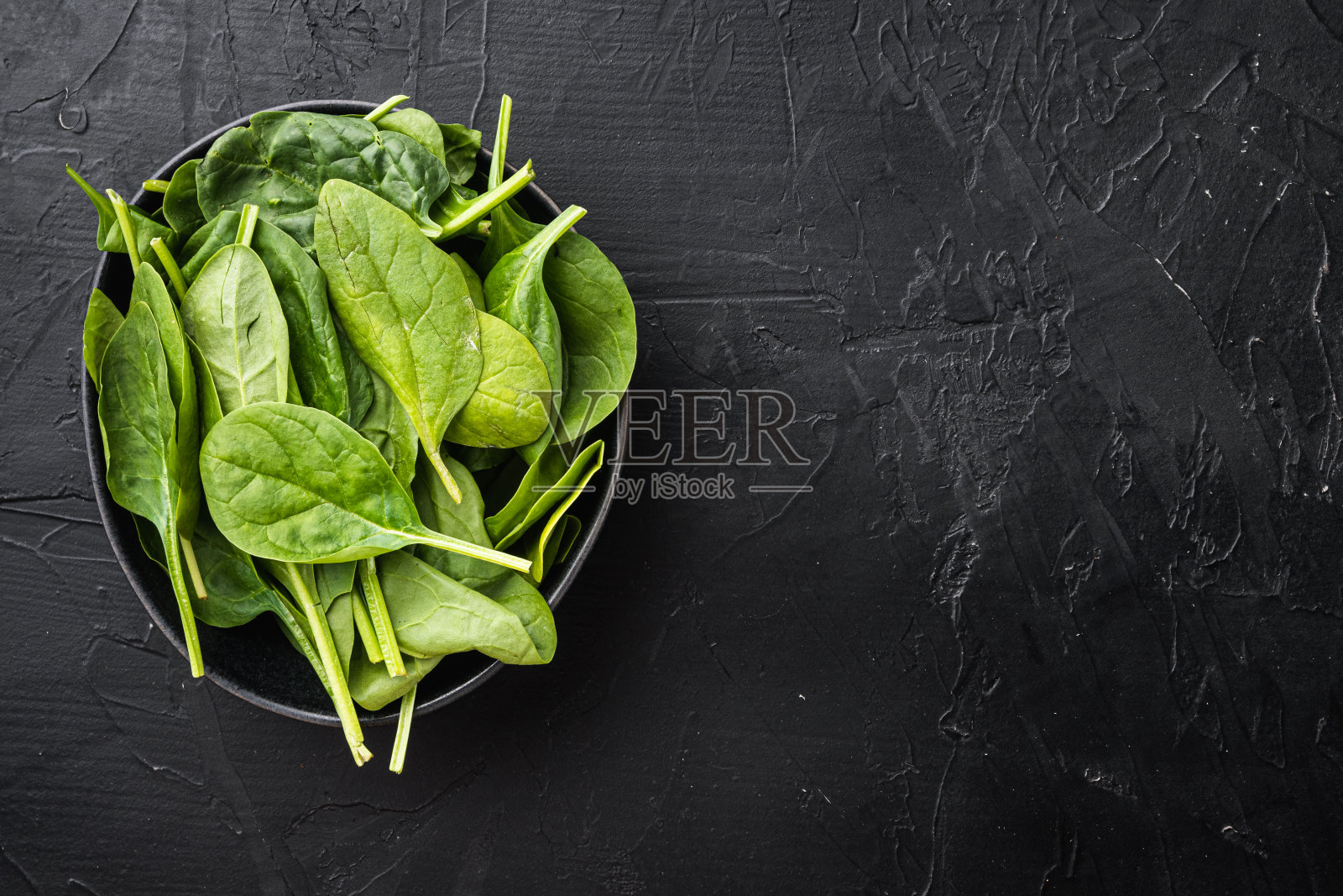 一捆新鲜菠菜,放在碗里,在黑色的石头背景上,俯视图平铺,有文字复制空间照片摄影图片