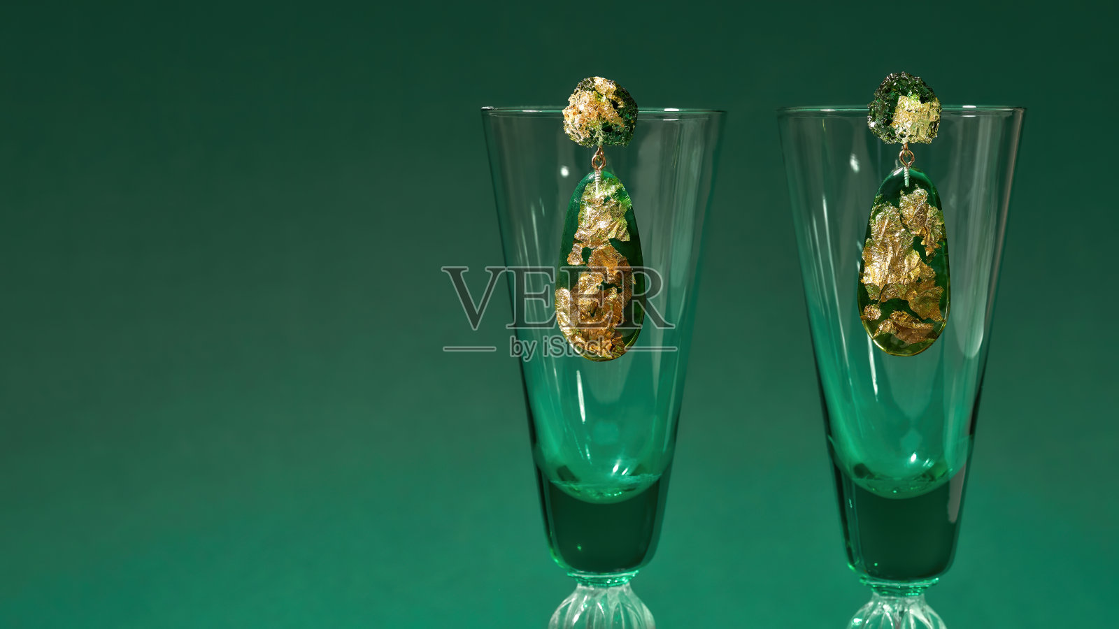 时尚手工制作的环氧树脂吊坠耳环的创意拍摄,在绿色的背景下孤立的葡萄酒杯上有金箔照片摄影图片