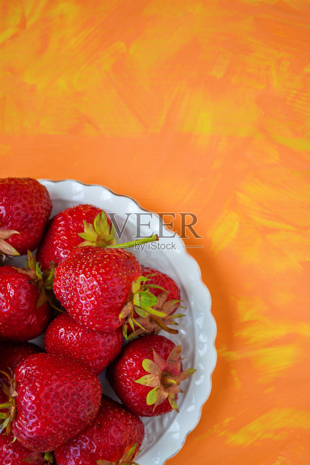 白色盘子上放着成熟的红草莓,背景是橙黄色照片摄影图片