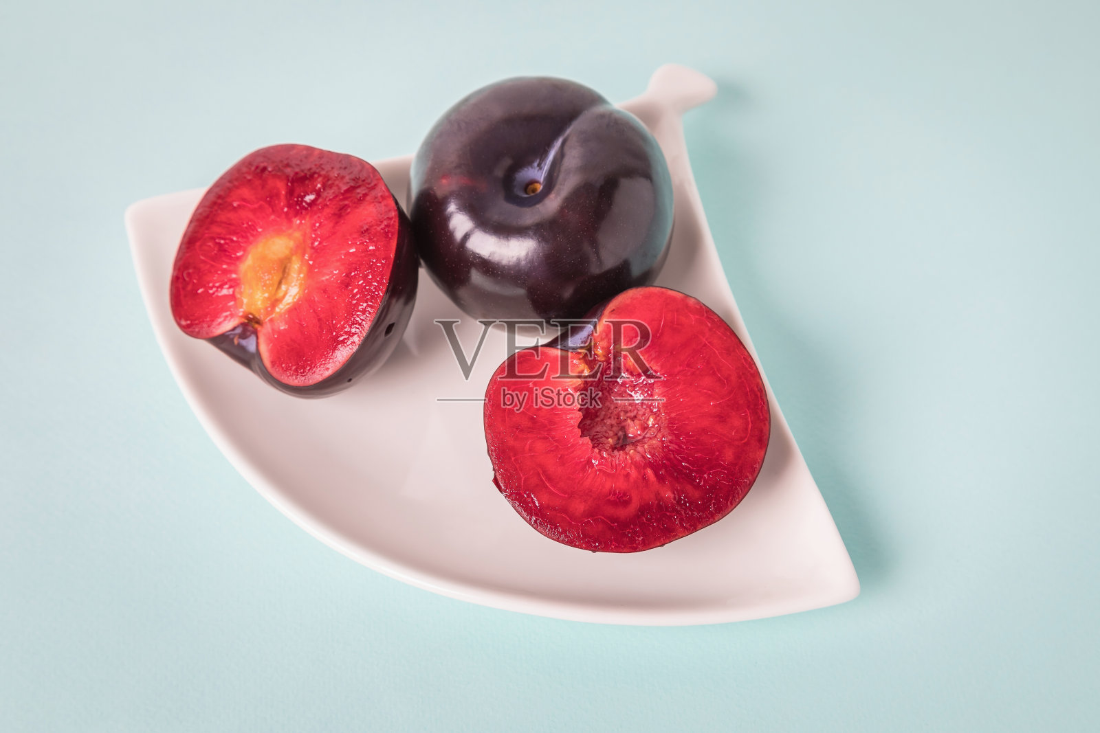 在一个白色的茶碟上放着一个大李子,把它切成两半,旁边放着一整个李子。照片摄影图片