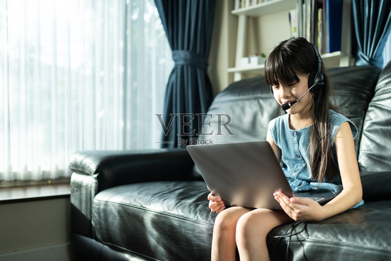 由于covid - 19大流行,亚洲小女孩通过数字远程会议向学校老师学习在线课程。孩子们在笔记本电脑上看虚拟视频会议,在家里学习。照片摄影图片