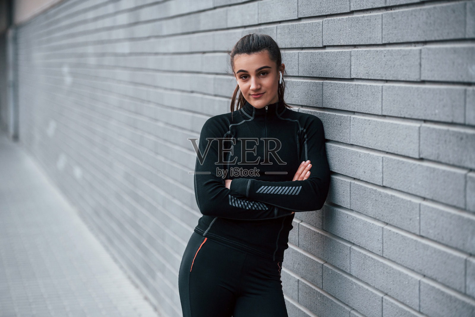 年轻的运动女孩在黑色运动服户外附近的灰色墙壁照片摄影图片