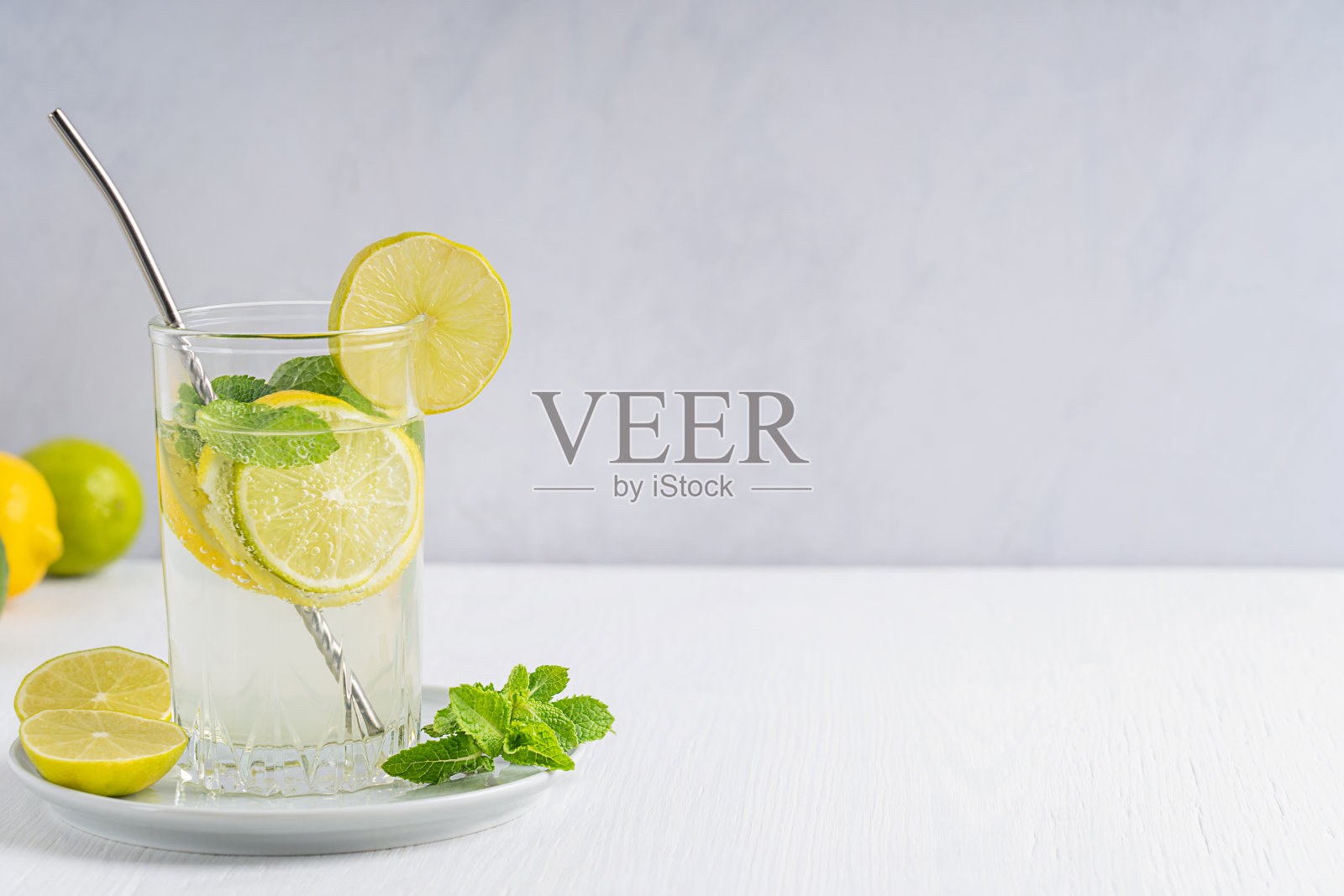 夏天,在白色的木桌上,喝一杯新鲜的自制柠檬水或莫吉托,配上酸橙和柠檬片,苏打水和薄荷叶,再配上稻草照片摄影图片