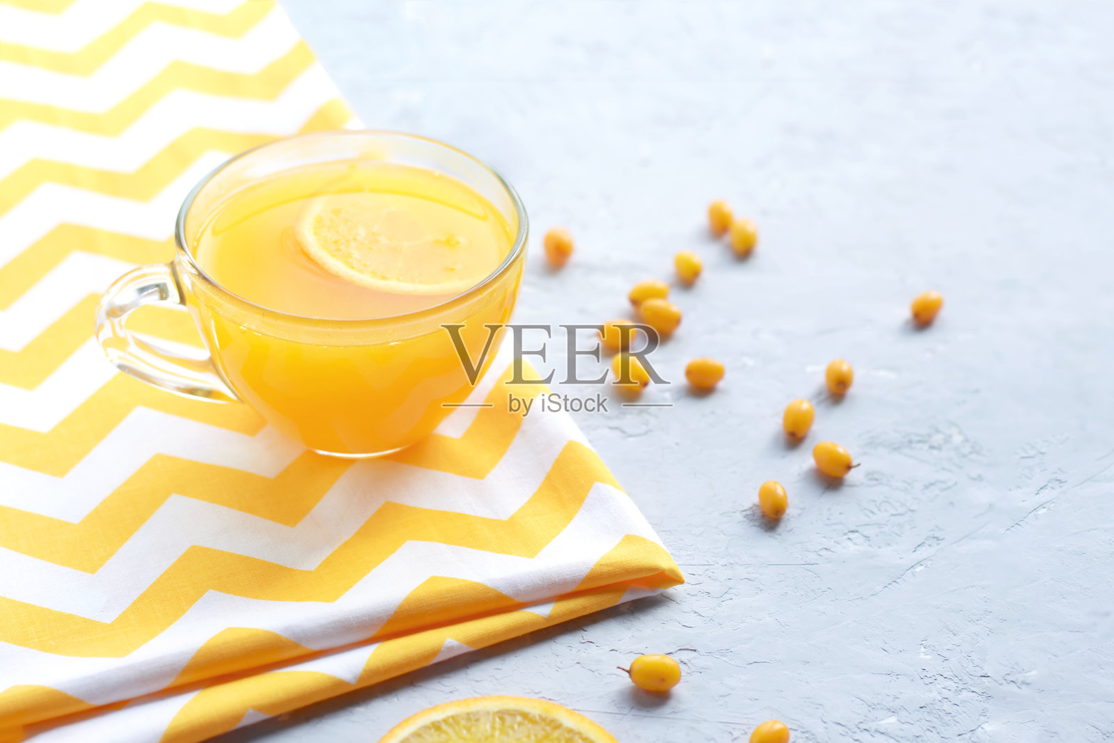 在灰色背景的透明杯子里放着沙棘和橙子的维生素茶。照片摄影图片