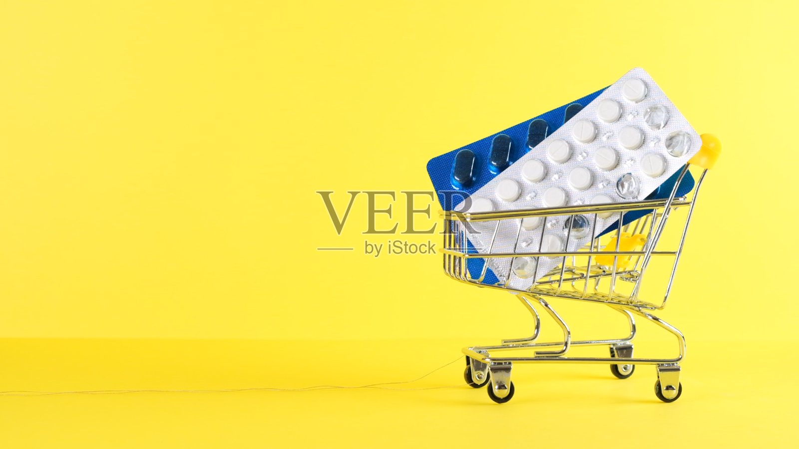 黄色背景下的购物车,特写。医学概念,网上购物照片摄影图片