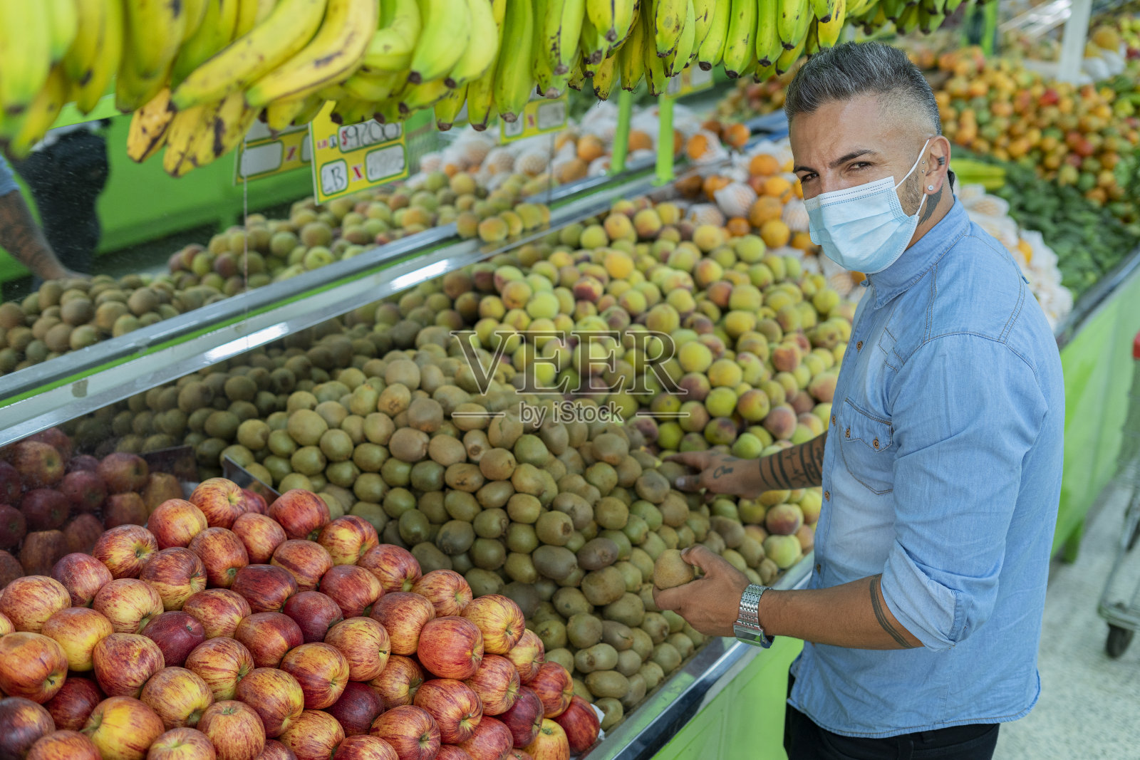 一名男子的肖像看着相机,同时显示他选择的水果,他正在选择放入购物车照片摄影图片