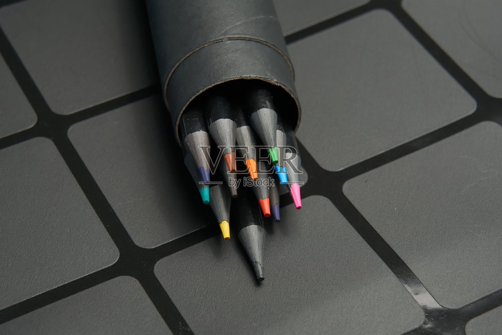 一套彩色铅笔,装在一个圆形的硬纸盒里,背景是黑色的。照片摄影图片