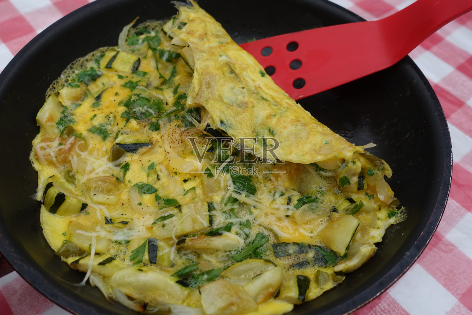 由切好的蔬菜、西葫芦、洋葱、青椒、平叶欧芹和磨碎的格鲁耶尔干酪制成的煎蛋卷照片摄影图片