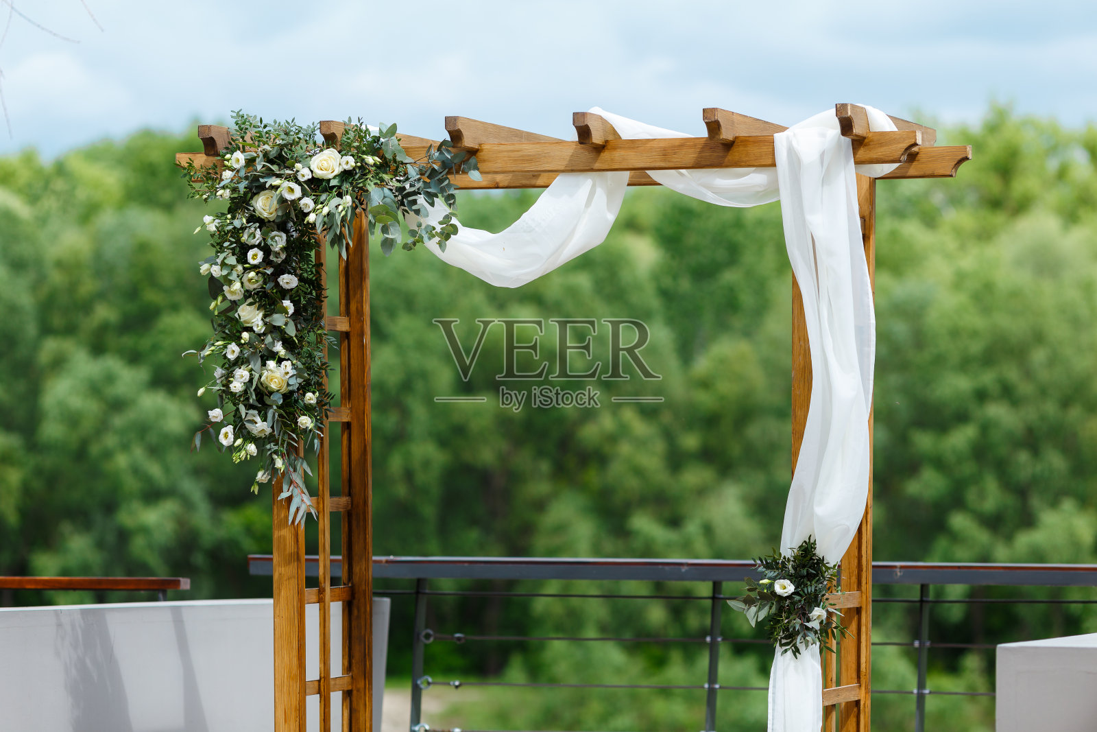 婚礼地点在码头附近的河边。木制的长方形拱门,白色的椅子上装饰着鲜花、绿叶、花瓣、桉树和薄纱。可爱,时尚的乡村装饰照片摄影图片