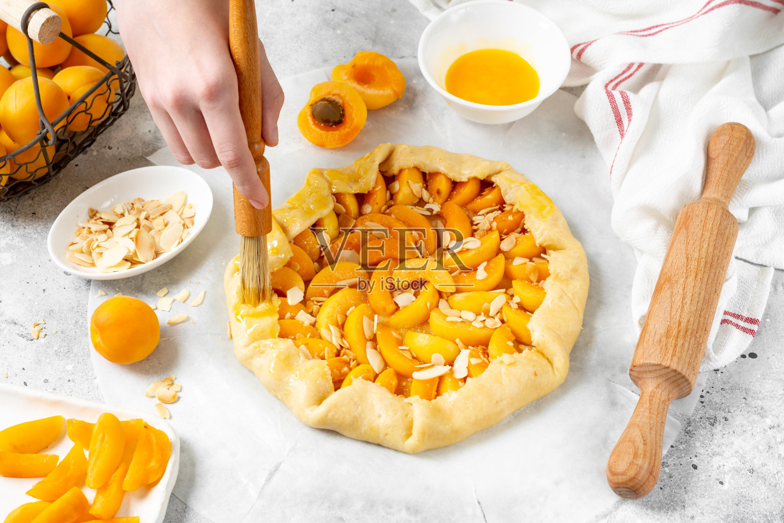 杏仁饼用杏和杏仁做法式酥饼或派的过程夏季烘焙的配料在一个轻的餐桌上的特写。在面团边缘涂上蛋黄。手在框架里照片摄影图片