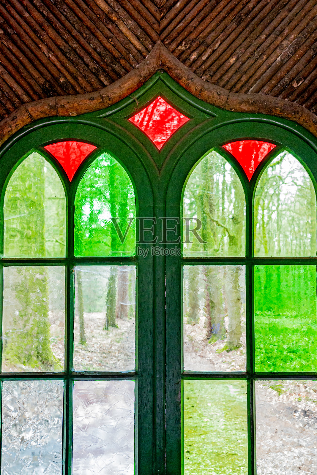 一个木制框架的窗户的特写,绿色和红色的玻璃,透过它们看到一条道路和树木照片摄影图片